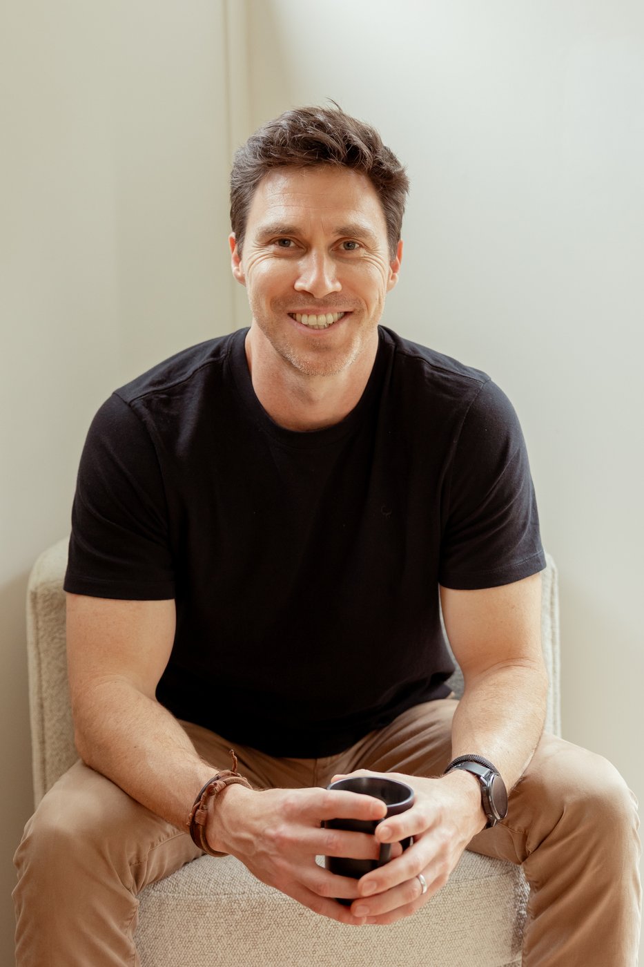 Justin King seated, holding a coffee mug and smiling